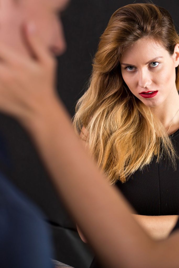 A woman looking at a man with an ulterior motive on her face and his face is being held emotionally by another woman